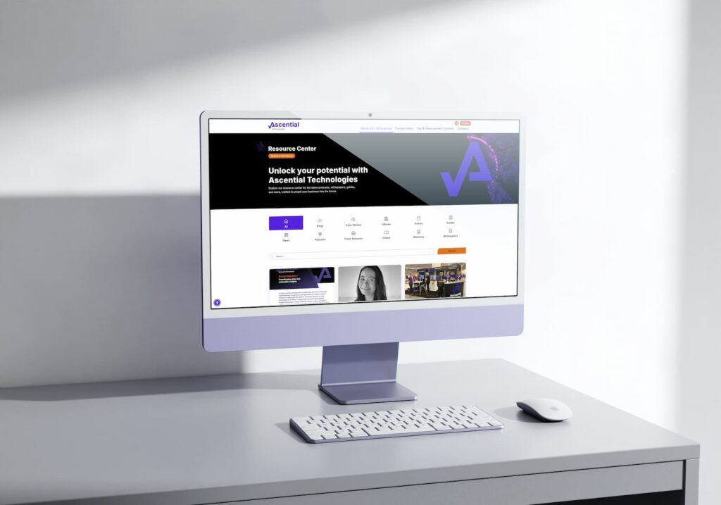 A desktop computer on a white desk displays the Ascential Technologies website homepage, featuring a header and navigation links.