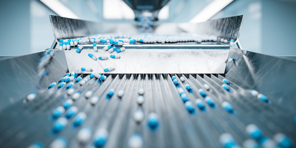 Close-up of blue and white capsules on a conveyor belt in a pharmaceutical manufacturing facility.