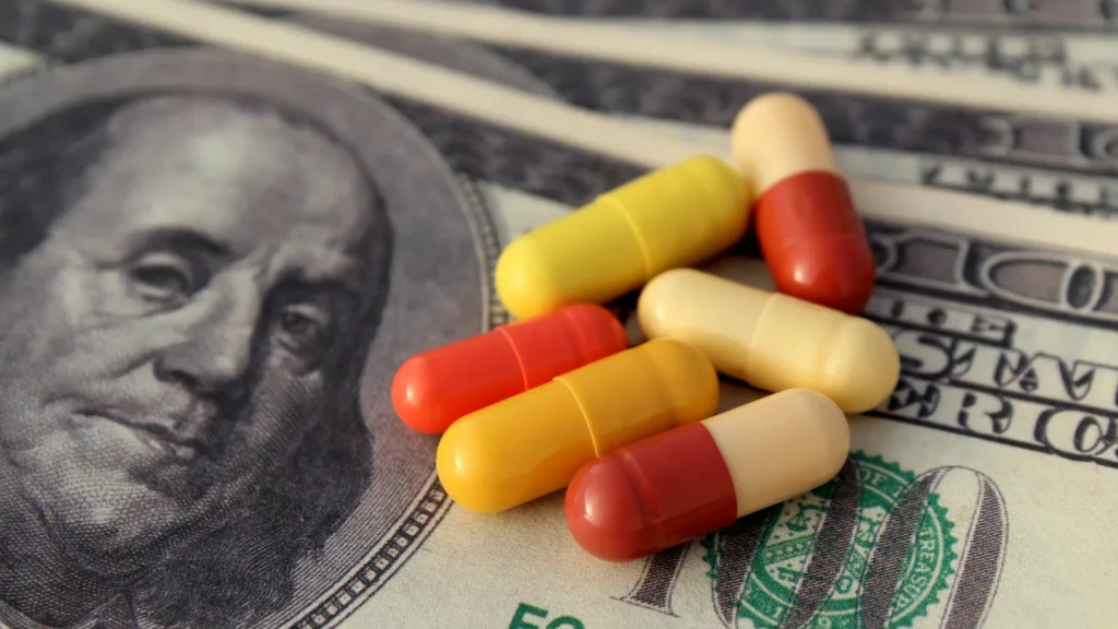 Several yellow and red capsules are placed on top of U.S. hundred dollar bills.