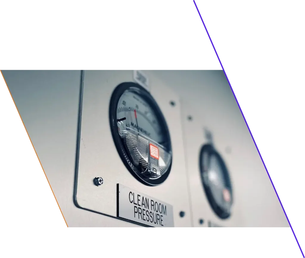 A close-up view of two industrial pressure gauges mounted on a wall, with one labeled "CLEAN ROOM PRESSURE.
