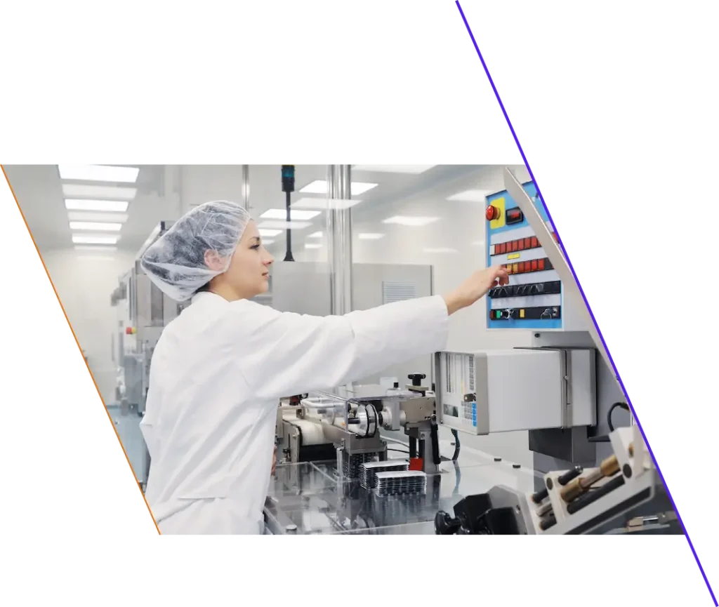A person in a lab coat and hairnet operates control buttons on industrial equipment in a laboratory or manufacturing facility.