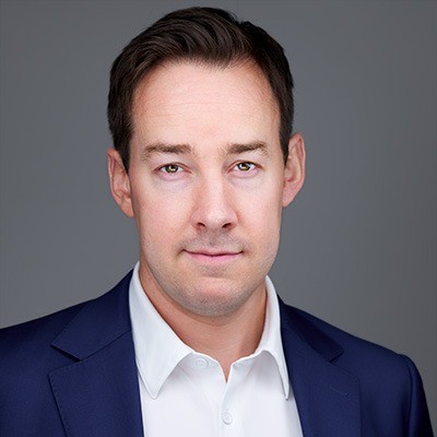 Professional man in a blue suit and white shirt against a gray background, looking confidently at the camera.