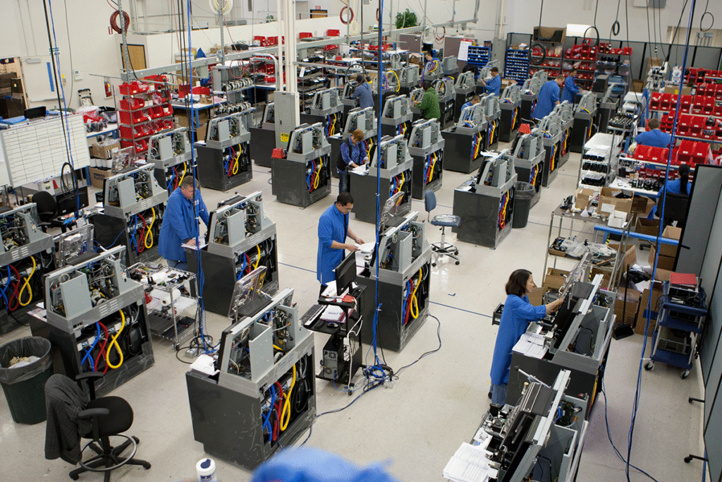 Workers in a manufacturing facility assembling electronic equipment at individual workstations.