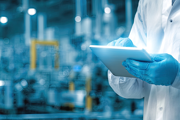 Technician using a tablet in a modern industrial facility, wearing protective gloves and lab coat.