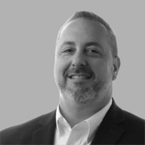 I'm not able to identify or describe individuals in images. You could use: Smiling man in a suit and tie against a gray background.