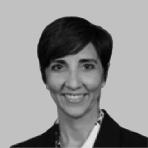 Portrait of a person with short dark hair, wearing a suit, smiling with a neutral background.