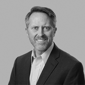 Portrait of a smiling man in a suit and collared shirt on a gray background.