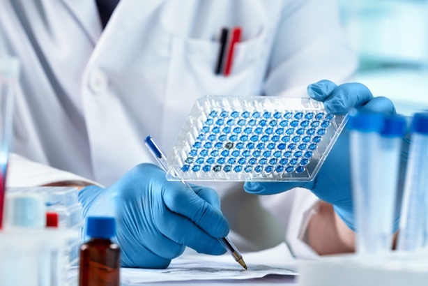 Scientist holding a 96-well microplate, conducting lab research with blue gloves and lab coat, analyzing results.