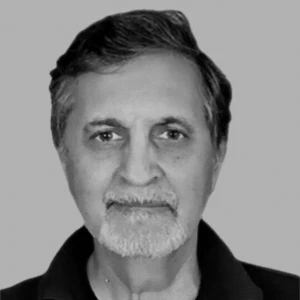 Portrait of an older man with a beard and short hair, wearing a dark shirt, set against a plain background.
